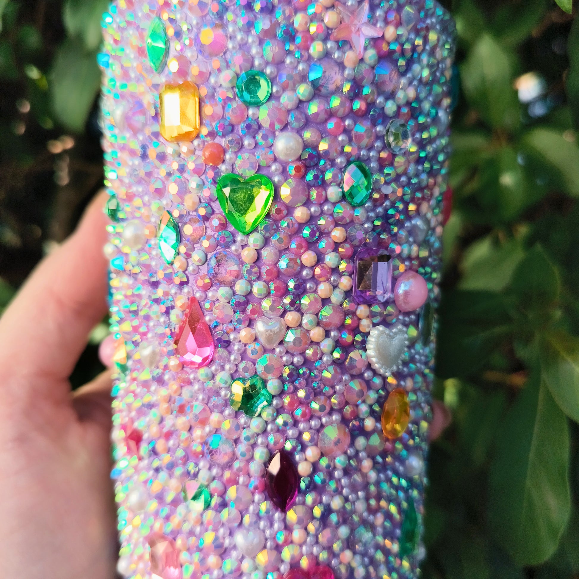 Drink tumbler with colorful gemstones held by a hand against a green leafy background