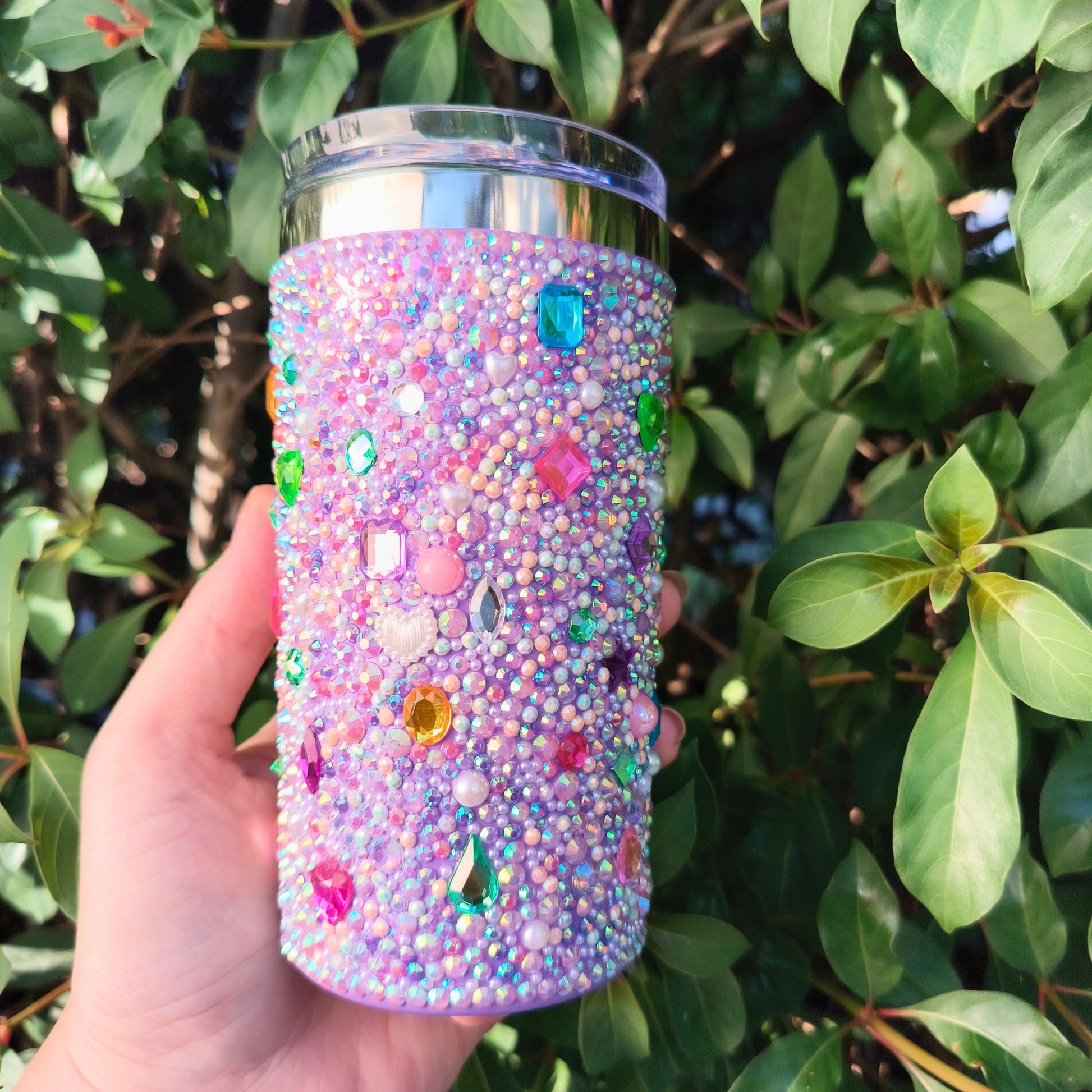 Hand holding a glittery tumbler in front of green foliage