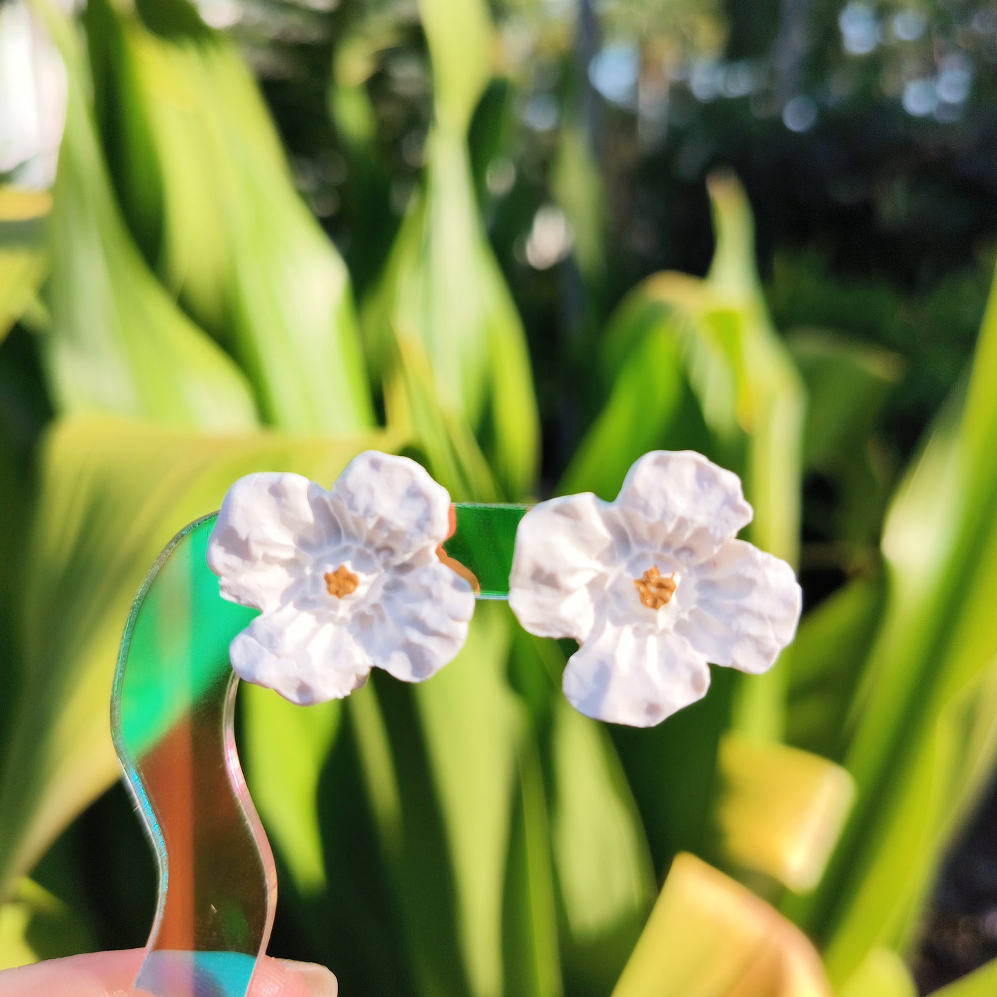 polymer clay magnolia bloom stud earrings with a plant background