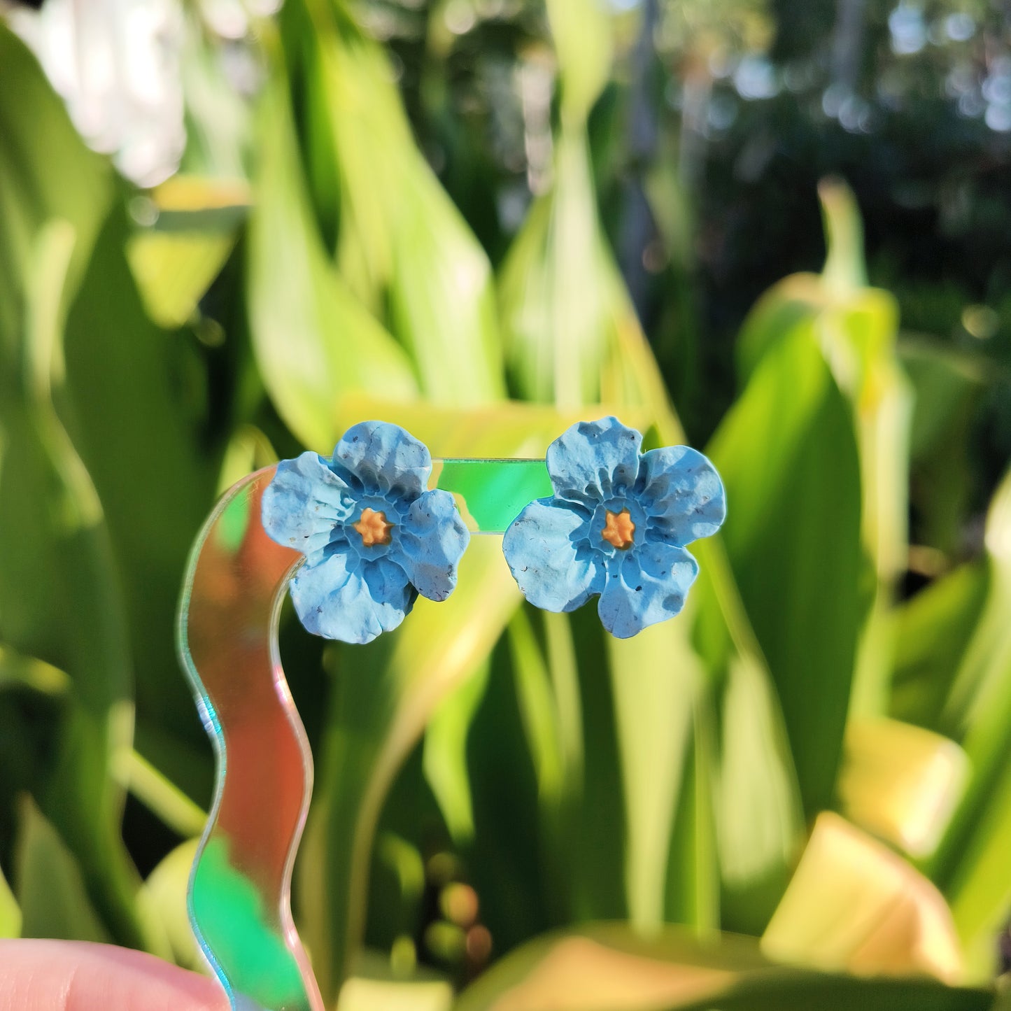 Blue flower earrings held against a green leafy background