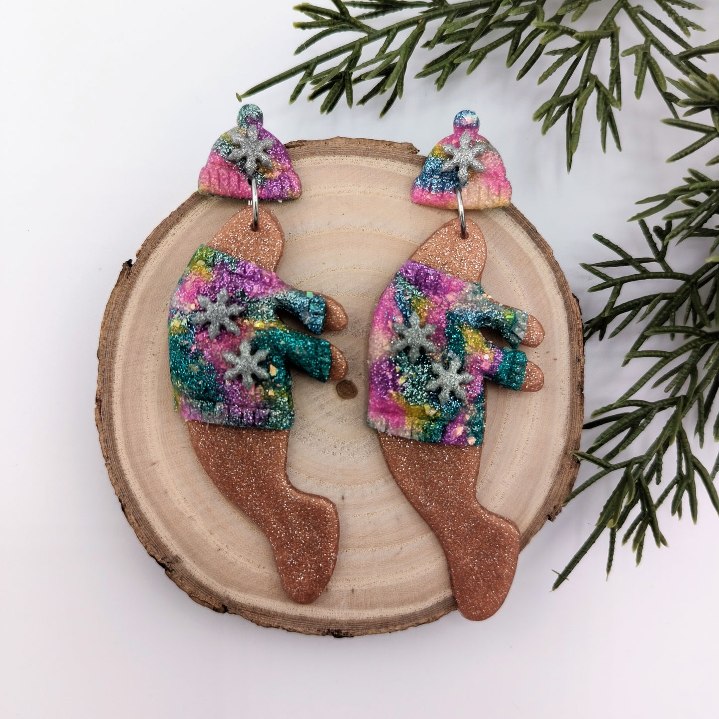 Colorful manatee earrings on a wooden slice with greenery