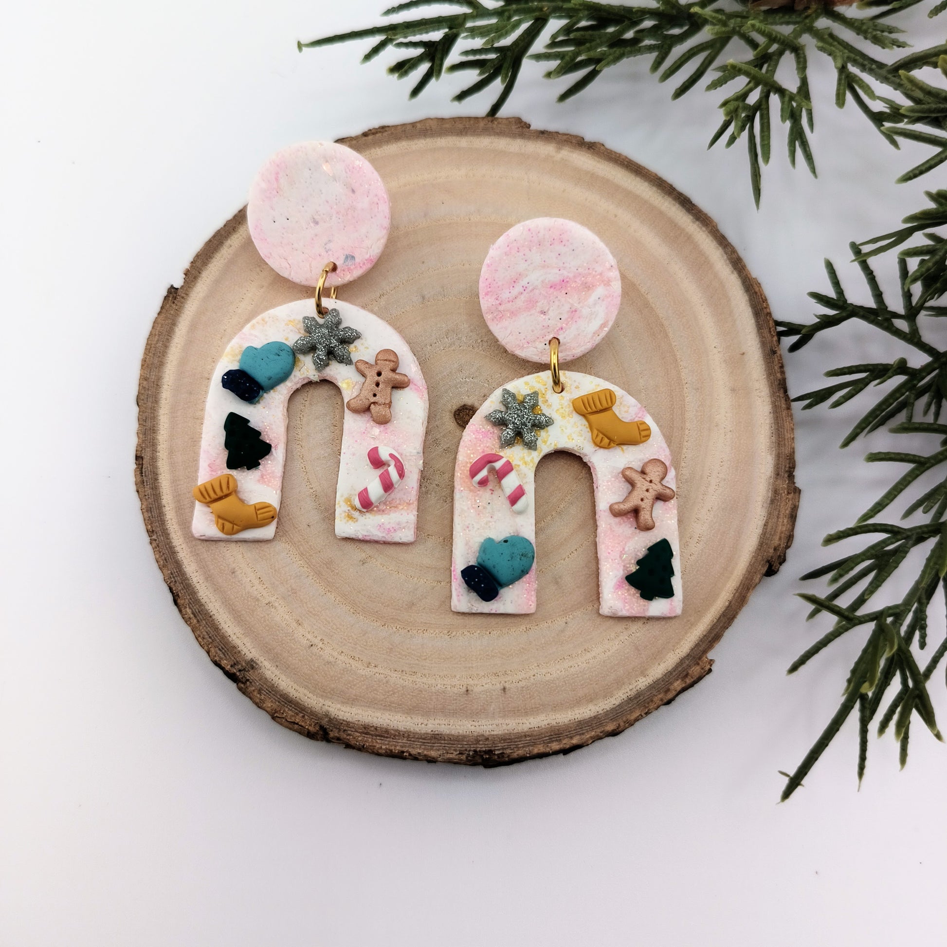 Decorative Christmas earrings on a wooden slice with greenery in the background