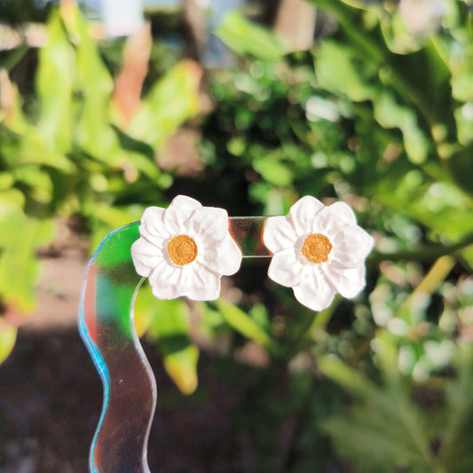 A pair of white daffodil stud earrings in natural lighting with greenery in the background.