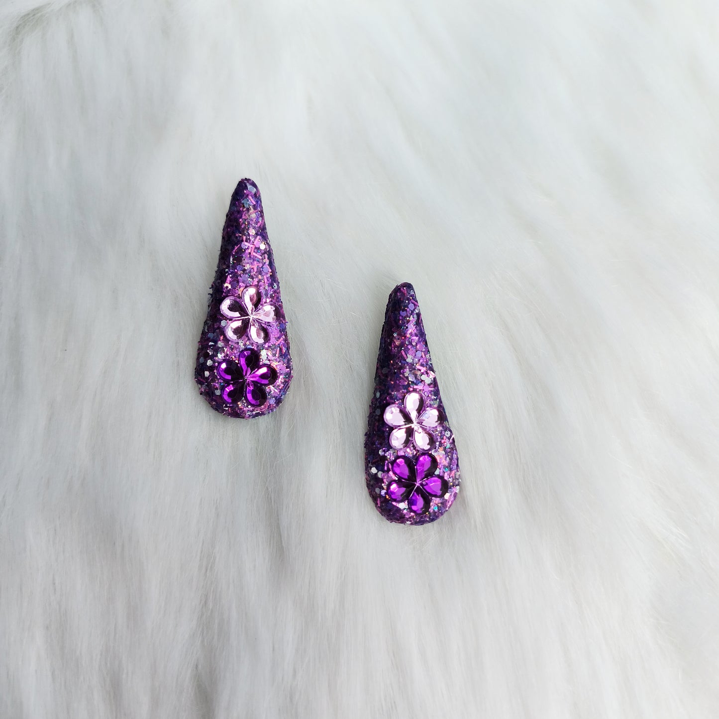 Purple teardrop-shaped earrings with floral designs on a white fur background