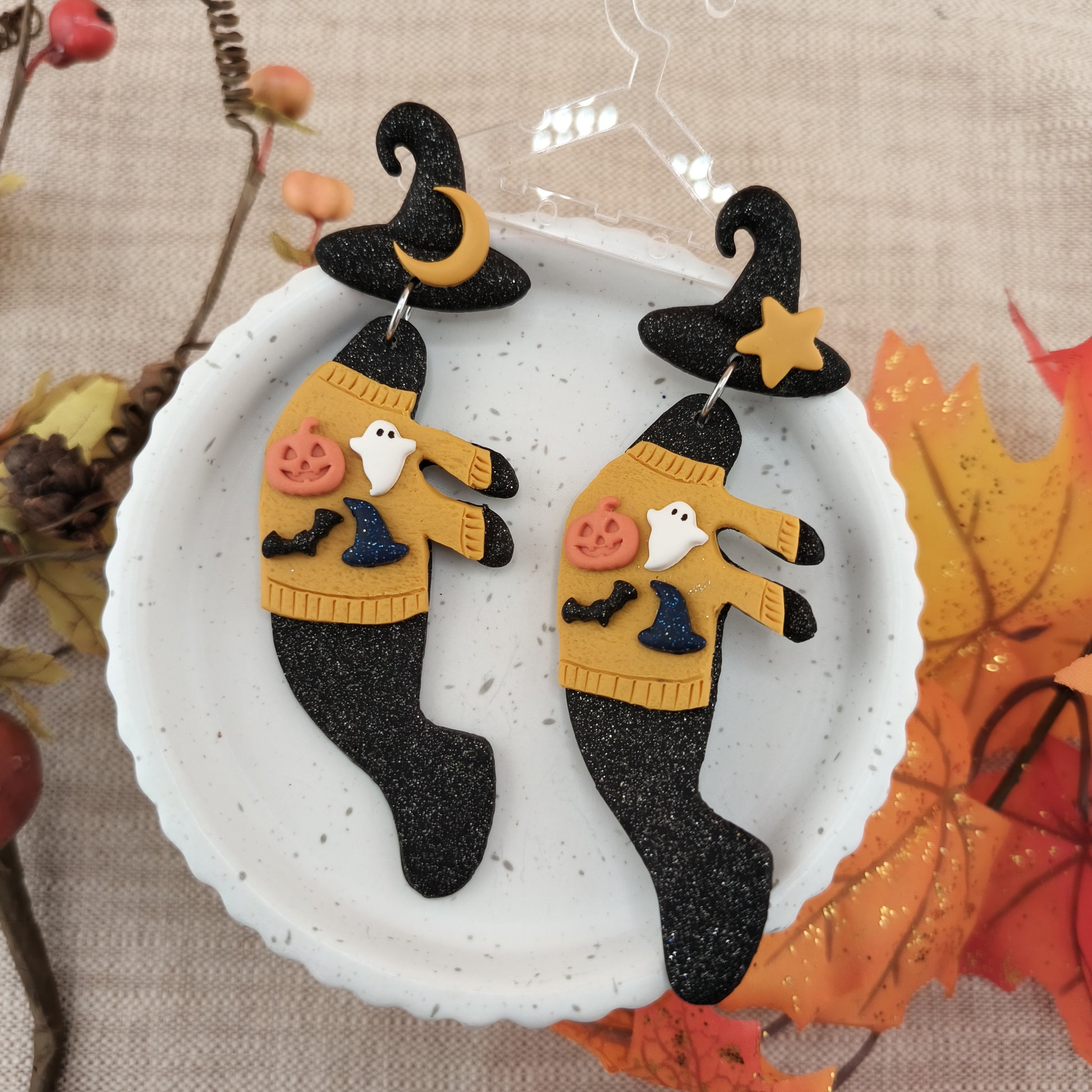 Halloween-themed manatee earrings with witch hats and sweaters on a decorative plate.