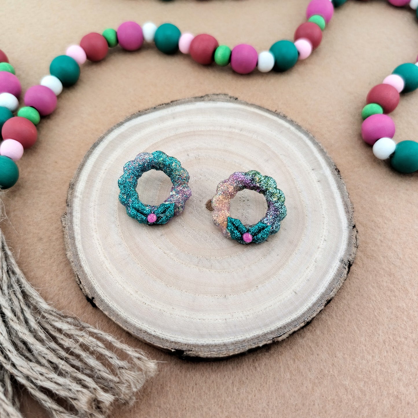 Colorful wreath shaped earrings on a wood slice with a beaded garland in the background/