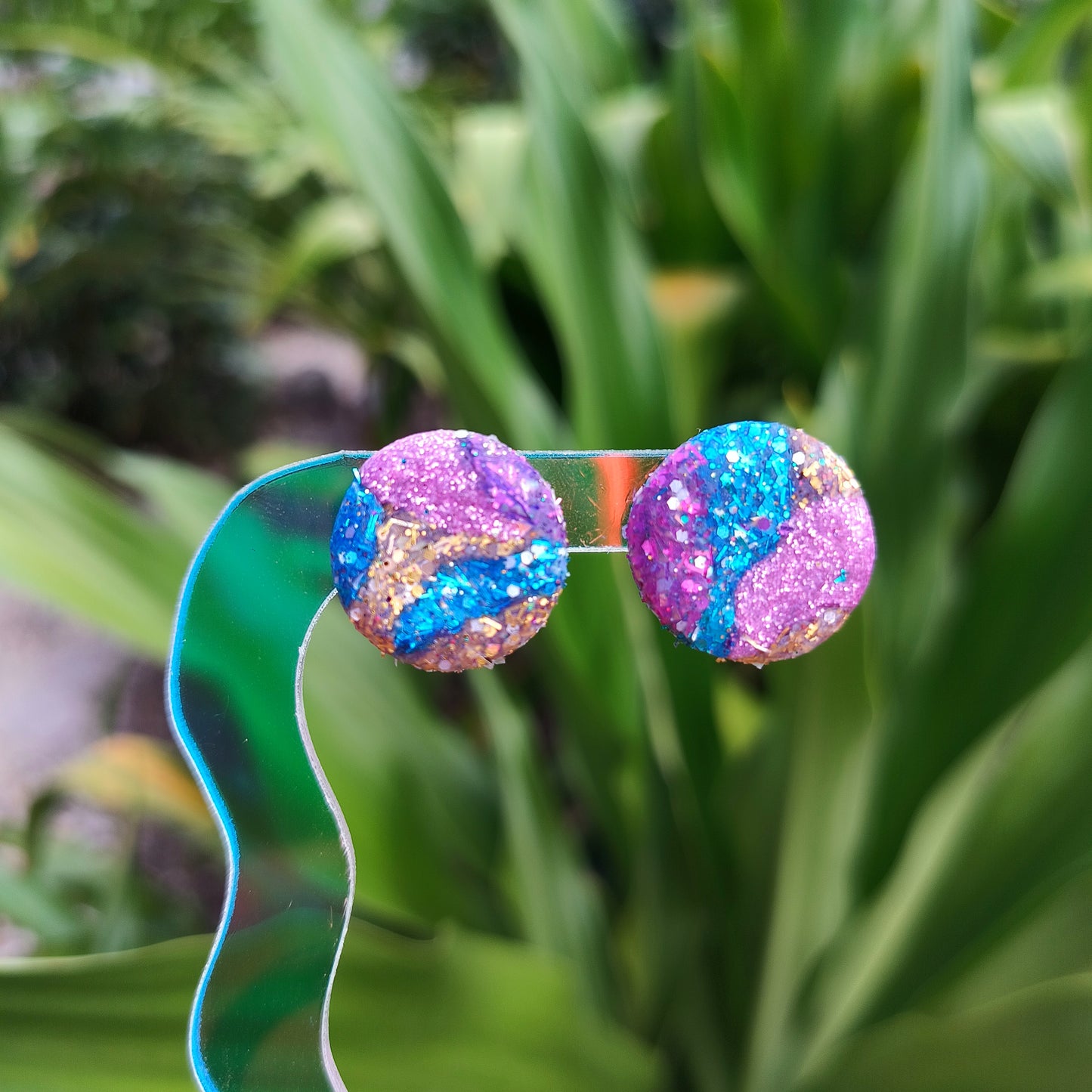 Colorful glittery earrings on a green ribbon with a blurred plant background
