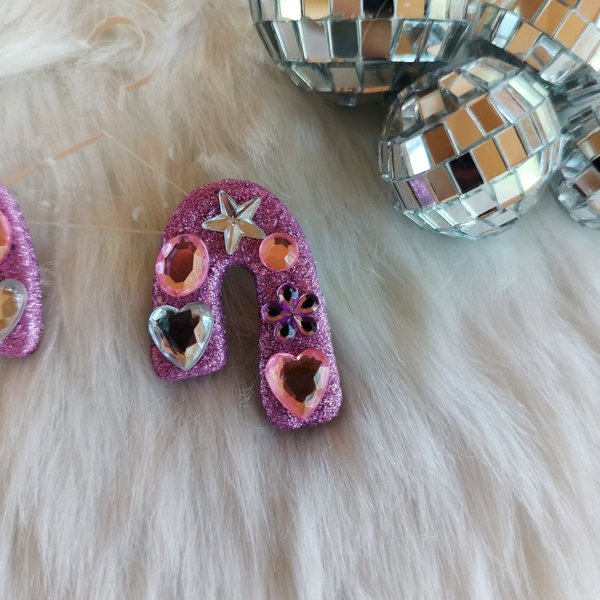 Stud earrings with pink glitter and decorative elements on a fluffy white surface.