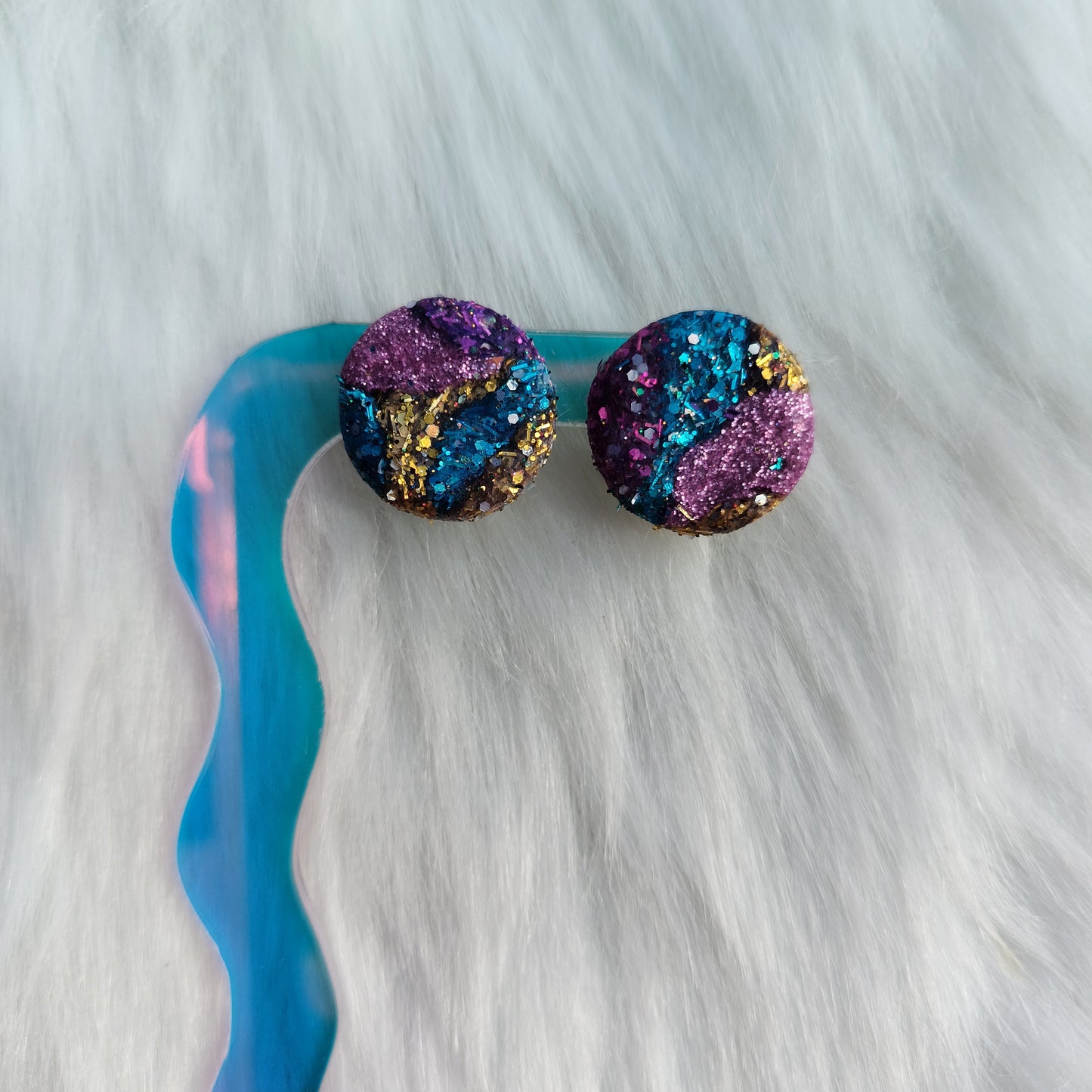 Multicolored glittery earrings on a white fur background