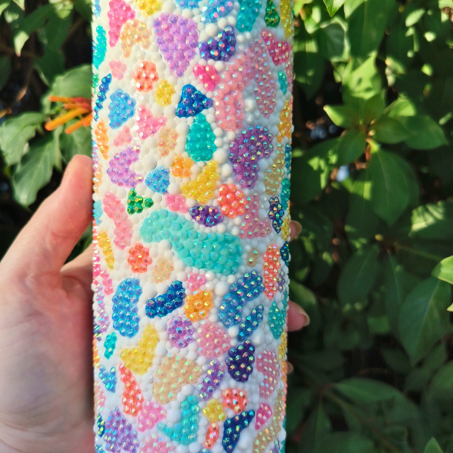 Colorful bedazzled drink tumbler held by a hand with a green leafy background